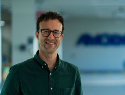 Electrical-engineering graduate Fintan Naughton is standing against a wall with a blue Amgen sign.