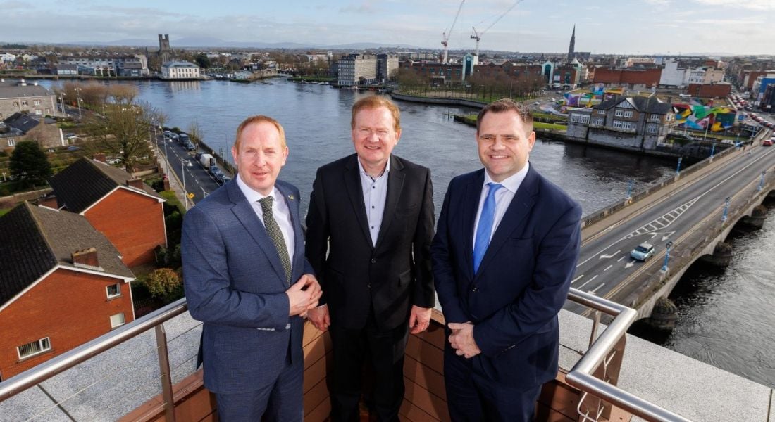 Three men standing on a balcony with views of Limerick city in the background.