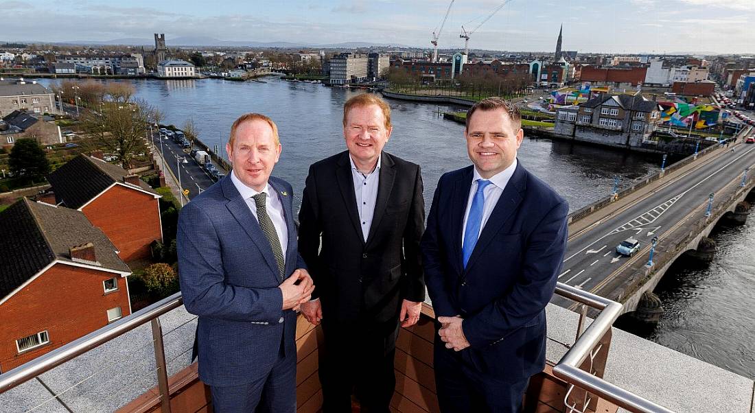 Three men standing on a balcony with views of Limerick city in the background.