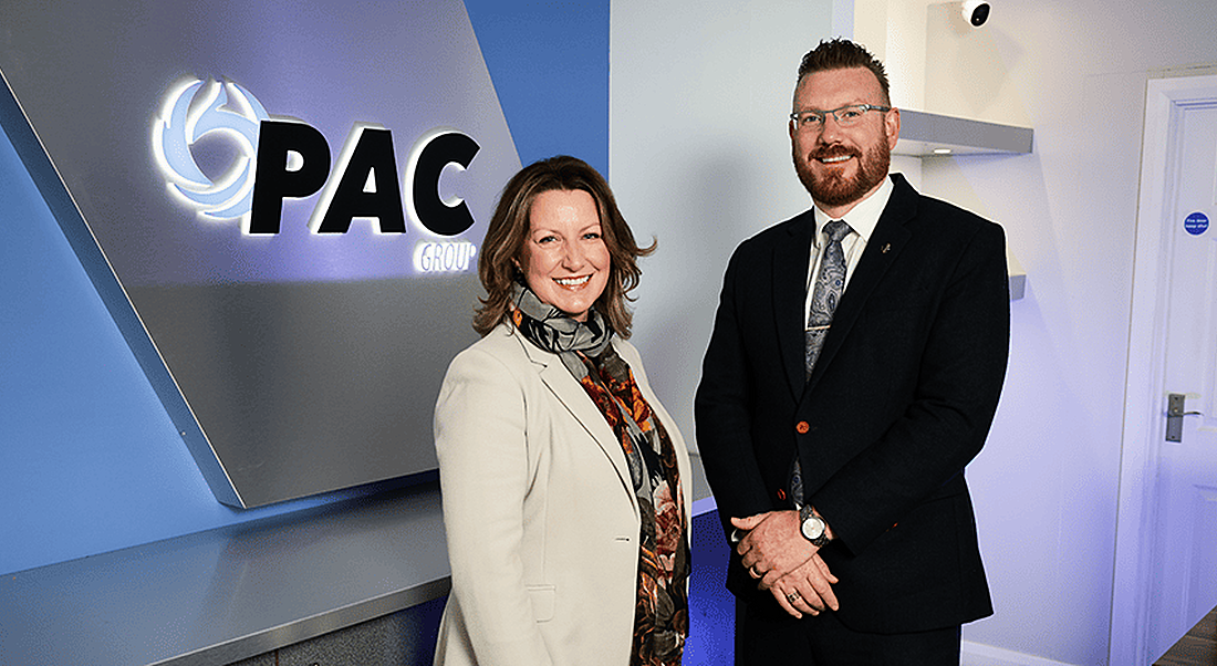 Photo of a woman and a man standing next to each other with the PAC logo on a wall behind them.