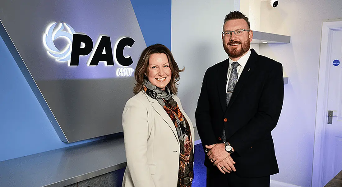 Photo of a woman and a man standing next to each other with the PAC logo on a wall behind them.