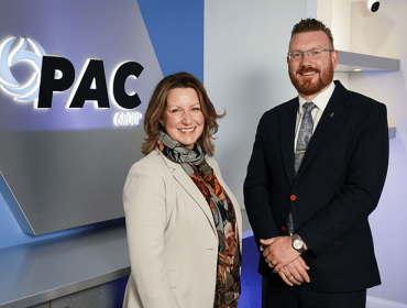 Photo of a woman and a man standing next to each other with the PAC logo on a wall behind them.