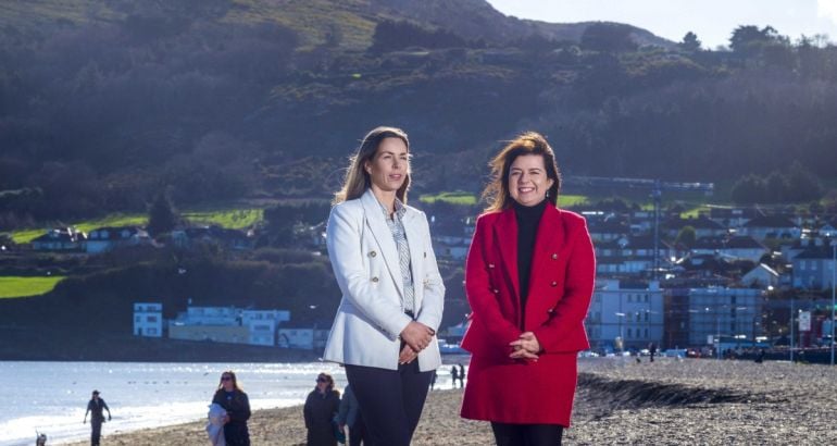 Two people from SD Worx Ireland, standing together on a beach with water and buildings of a town in the background.