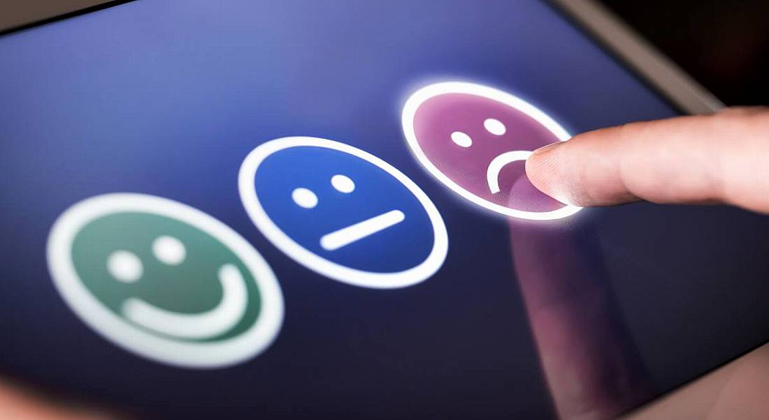 A trio of faces on a screen representing emotions from happy to sad as a person's finger points at the sad face.