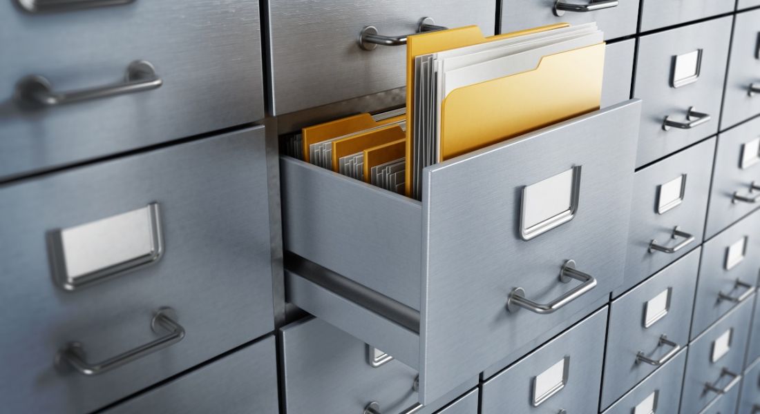 A folder containing files sticks out of an opened drawer of a grey filing cabinet.