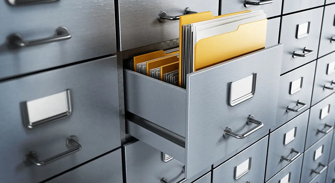 A folder containing files sticks out of an opened drawer of a grey filing cabinet.