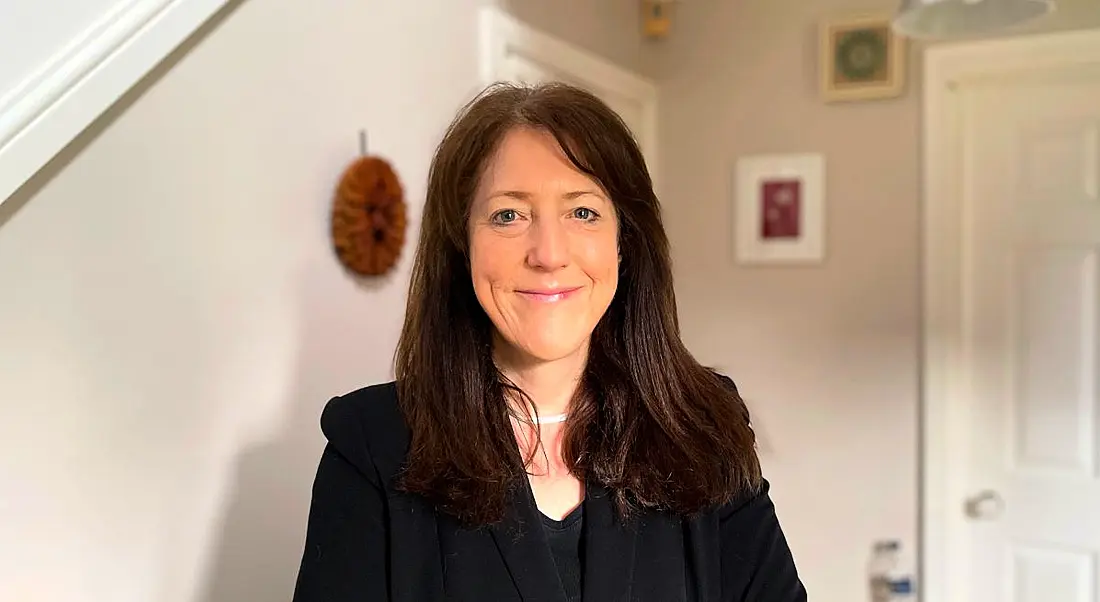 A woman with long brown hair wearing a dark blazer smiles at the camera. She is Karen MacGregor.