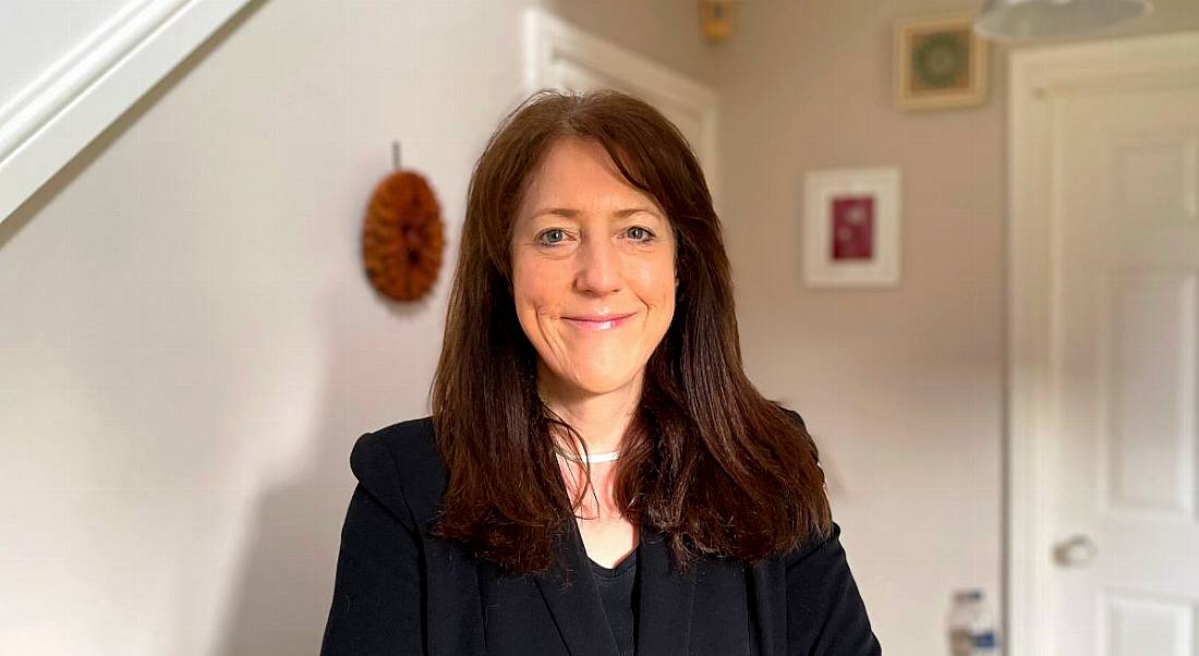 A woman with long brown hair wearing a dark blazer smiles at the camera. She is Karen MacGregor.