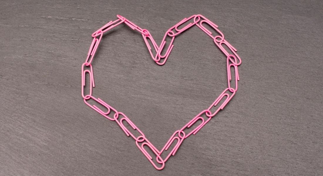 A bunch of pink paperclips intertwined and put into the shape of a love heart on a table to symbolise romance at work.