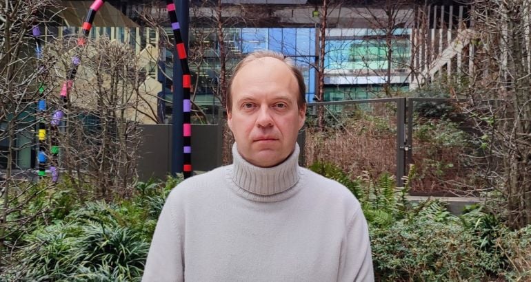 A man wearing a cream coloured turtleneck stands in a garden outside an office building. He is Oleksiy Ryabchuk, a senior software engineer at Integral Ad Science.