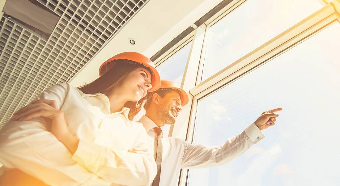 Two engineers standing beside a window with the sunlight illuminating them. One of them is pointing out the window.