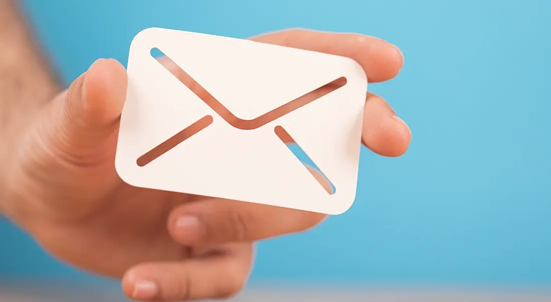 A hand holding a white email icon envelope against a blue background.