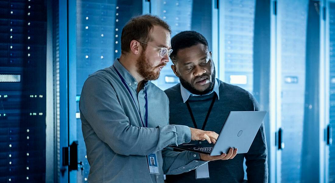 Two engineers discussing something and looking at a laptop in a data centre control room.