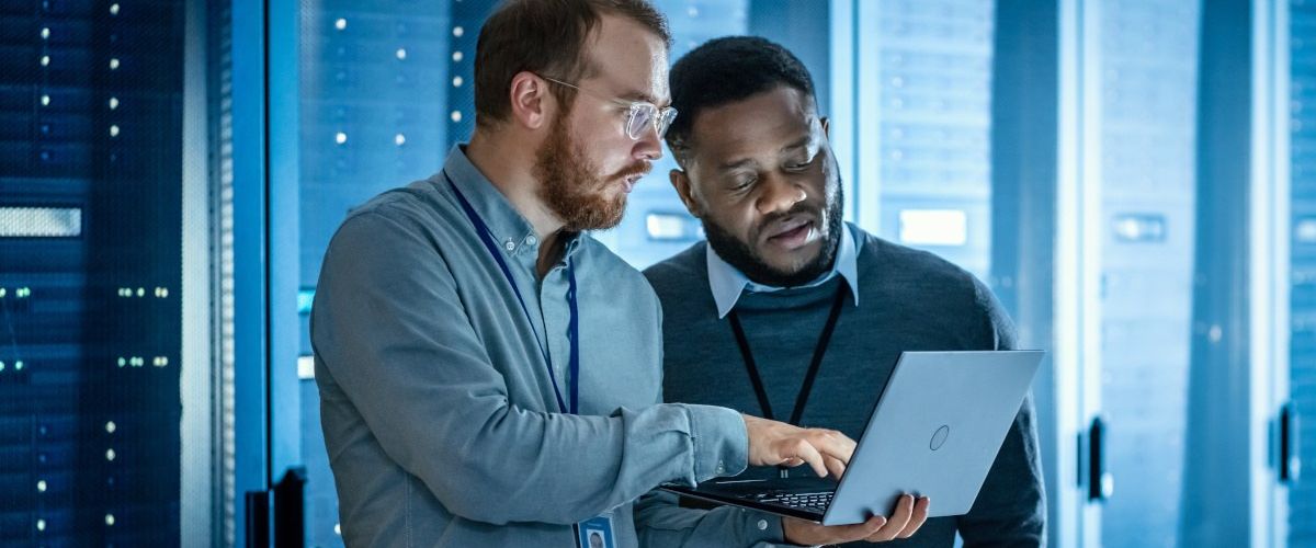 Two engineers discussing something and looking at a laptop in a data centre control room.