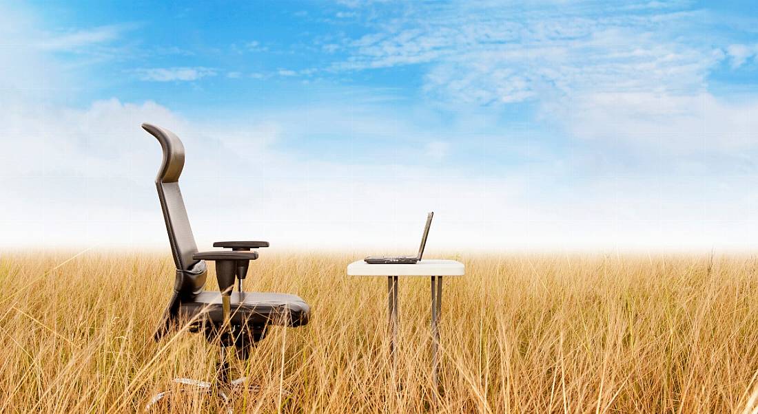 Remote working office in a field concept showing an office chair and a desk in the middle of a wheat field.