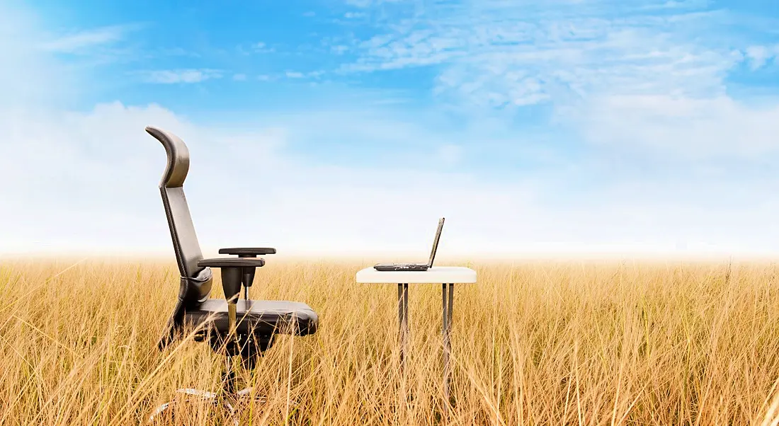 Remote working office in a field concept showing an office chair and a desk in the middle of a wheat field.