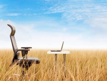 Remote working office in a field concept showing an office chair and a desk in the middle of a wheat field.