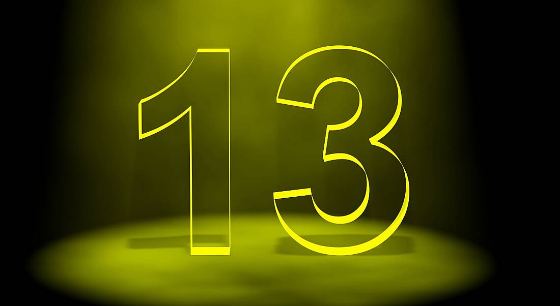 The number 13 in black lit up by yellow light on a black background.