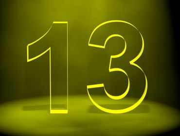 The number 13 in black lit up by yellow light on a black background.