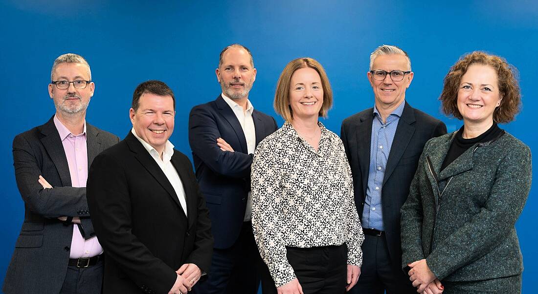 Six people from BearingPoint standing in a row with a blue background.