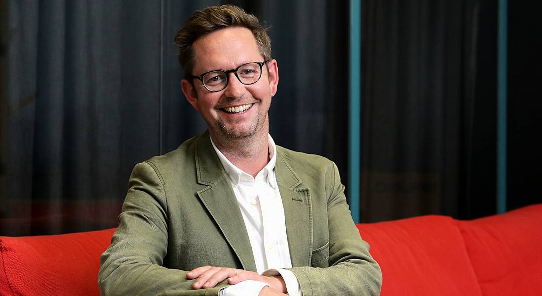 Jonathan Boakes sitting on a red sofa, leaning forward slightly for the camera.