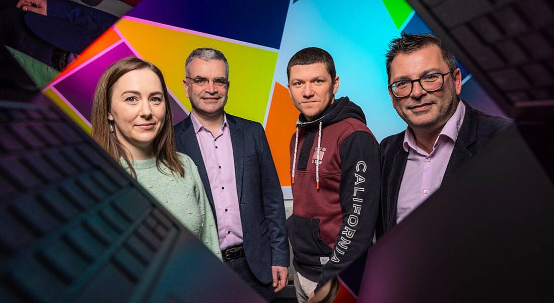 Four people facing the camera through a walled design that makes them look as though they are looking through broken glass.