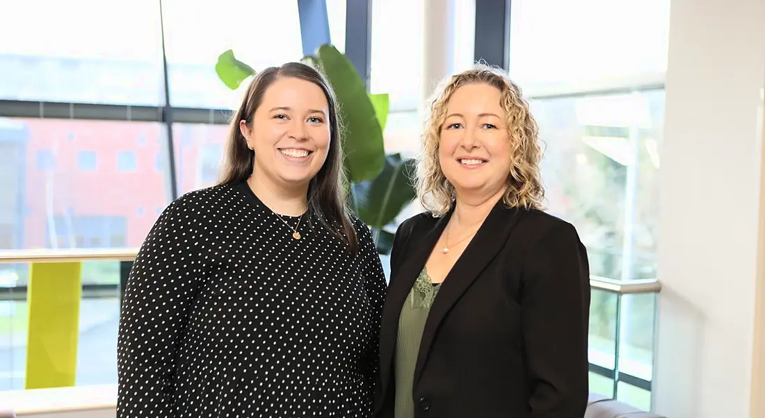 Two women stand together smiling in an office. They are Emer Guinane and Sharon Walsh of Fidelity Investments.