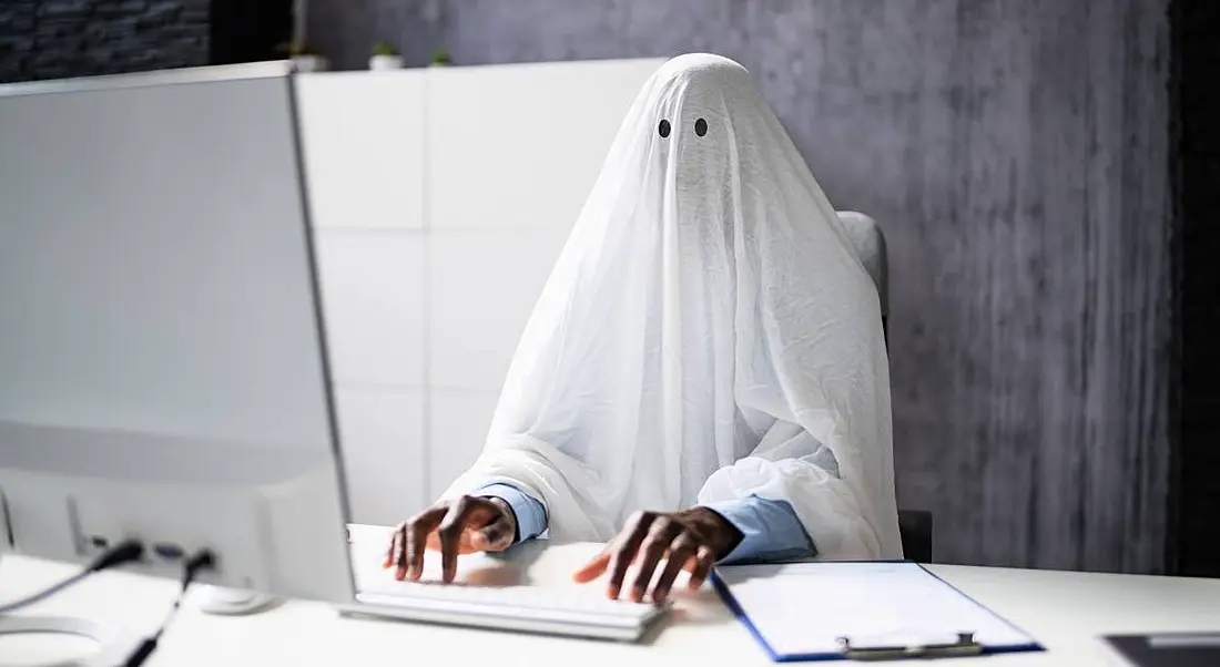 A man in a ghost costume works on a laptop.