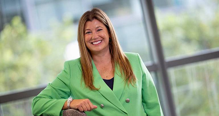 A woman in a green blazer leans on a grey wall in front of an out-of-focus window. She is the MD of Optum UK and Ireland.