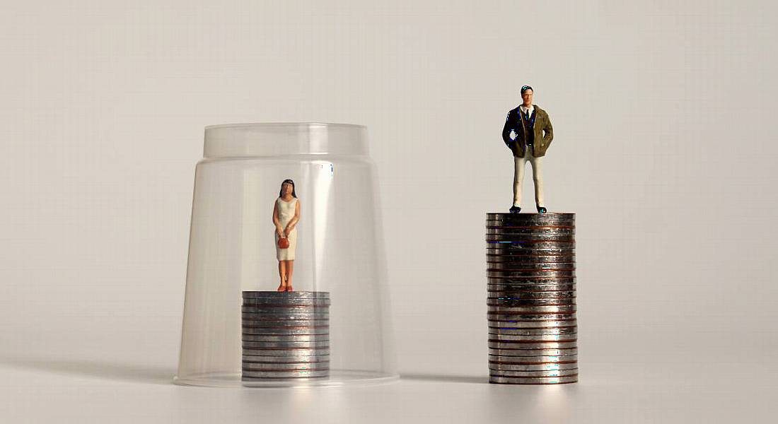 A toy man and woman standing on coins showing that the woman is trapped under a glass ceiling, preventing growth.