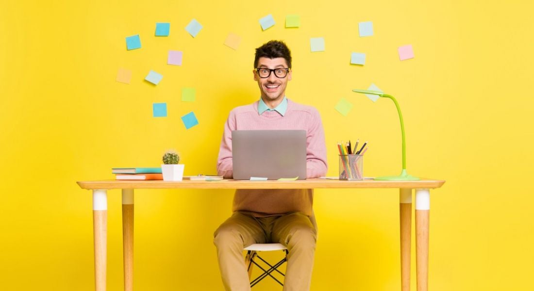 A happy man against a yellow background, at his work computer.