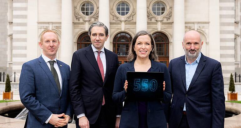 Three men and a woman in business attire stand in a line. The woman holds a tablet that shows the number 550 in blue writing.