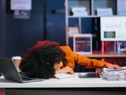 View of young woman in glasses with her hands on her head and brow furrowed with stress, poring over work.