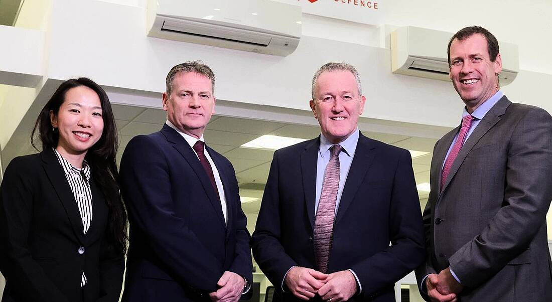 Four people - a woman and three men- dressed in professional business attire smile for a photograph.