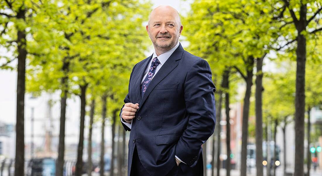 Managing director of Expleo Ireland, Phil Codd stands in a suit in front of a tree-lined road.