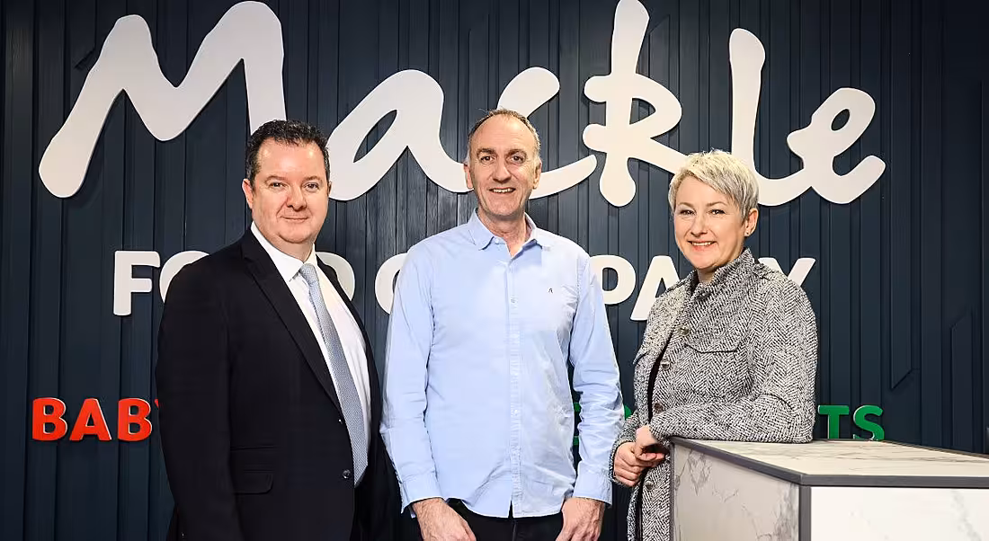 Two men and a woman stand in front of a sign that says Mackle.