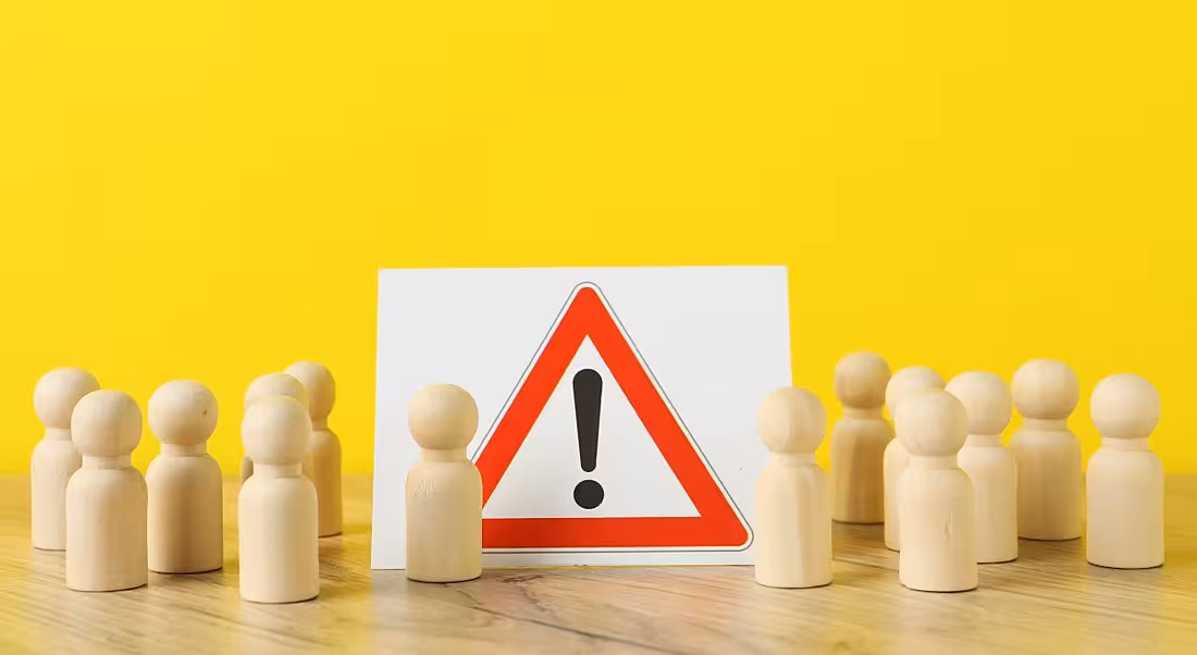 Wooden figures and a white and red warning sign against a yellow background.