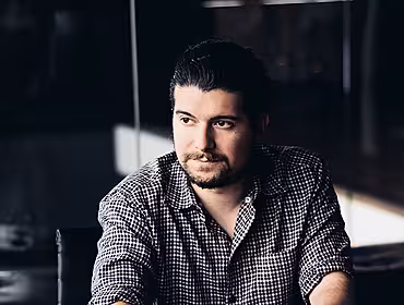 A man wearing a check shirt with sleeves rolled up looking off to the left. He is the founder of Squarespace.