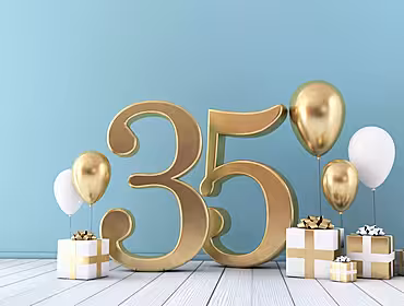 The number 35 in gold with presents and balloons in gold and white on a floor in front of a turquoise wall.