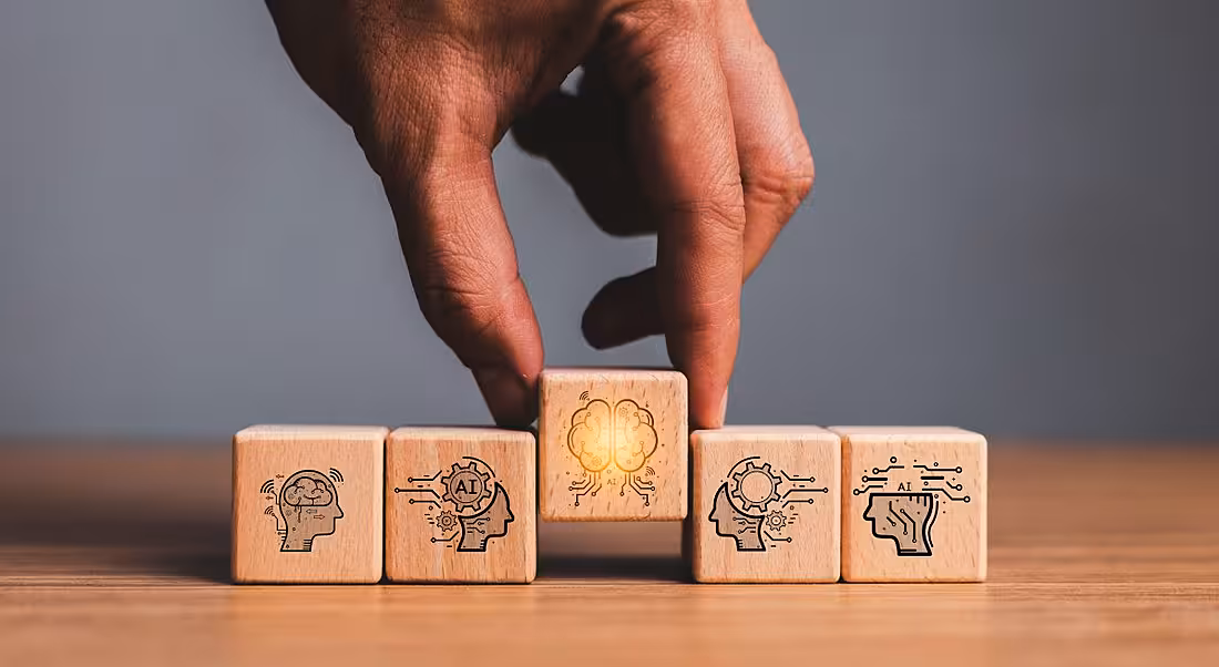 A hand selects a wooden block with iconography related to organisational AI.
