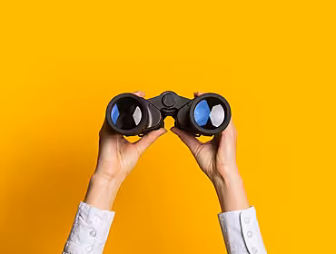A yellow background, with a pair of hands holding up binoculars.