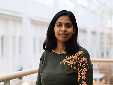 A headshot of a young woman wearing a green jumper standing in a brightly lit office.