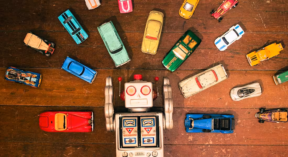 An aerial image of a toy robot lying on a wooden floor. It is surrounded by toy cars to symbolise driving the AI revolution.