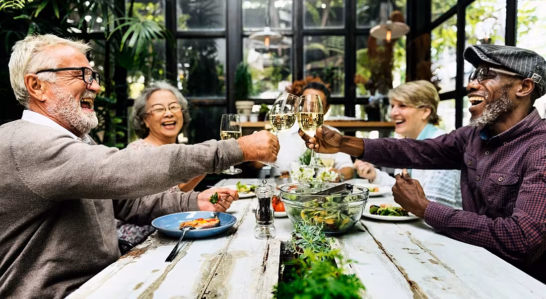 Representing retirement, older people clink glasses and enjoy a meal together.