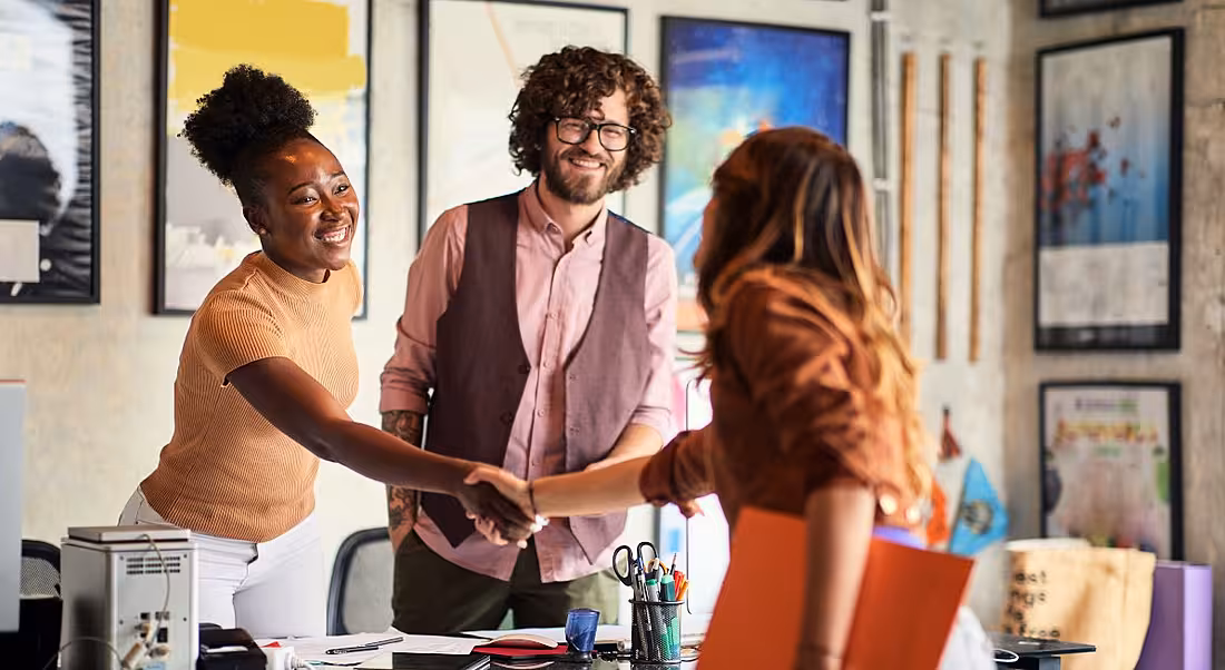 Two women shake hands as a man looks on, in what seems to be a job interview.