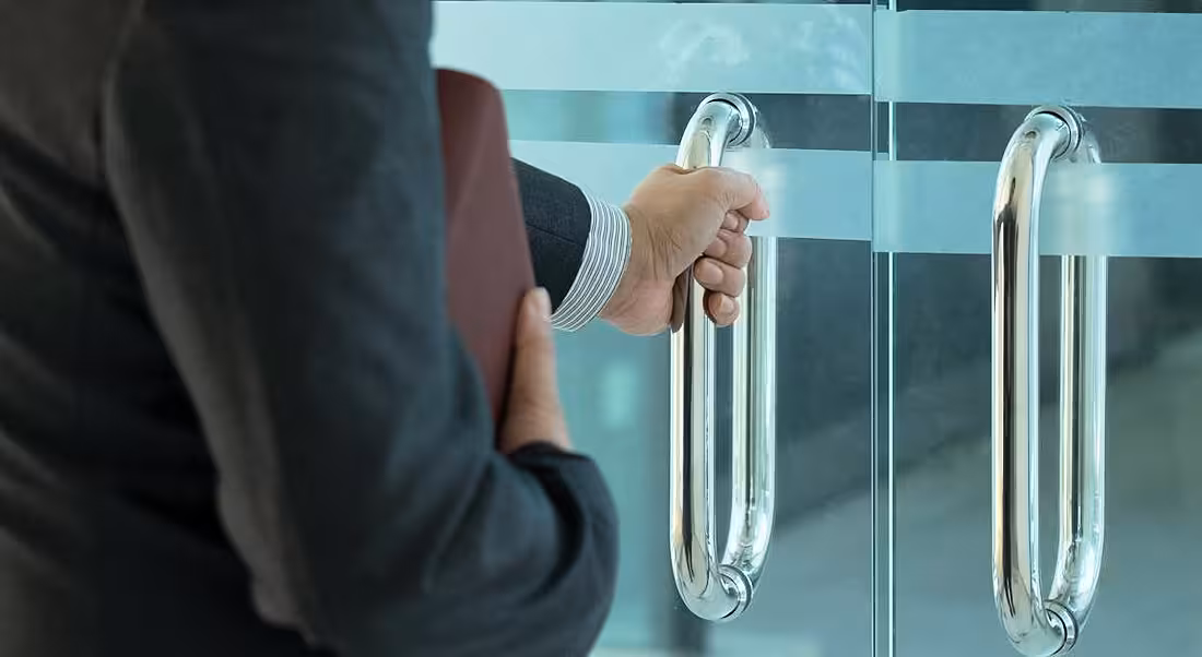 A man in a grey suit with a red folder has his hand on a door, about to open it.