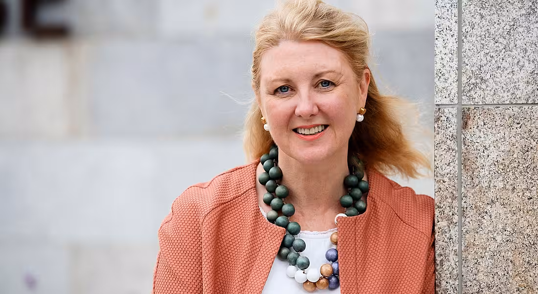 Maria Cullen of MSD is standing against a grey wall outdoors and wearing a pink blazer while smiling into the camera.
