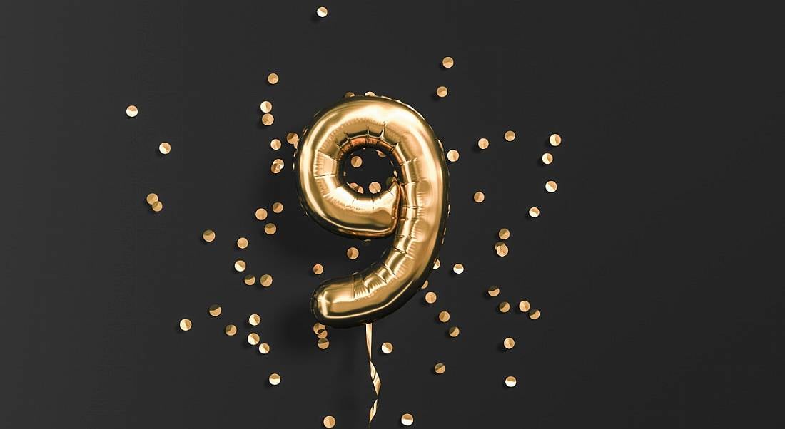 Number nine gold foil balloon and gold confetti on black background.