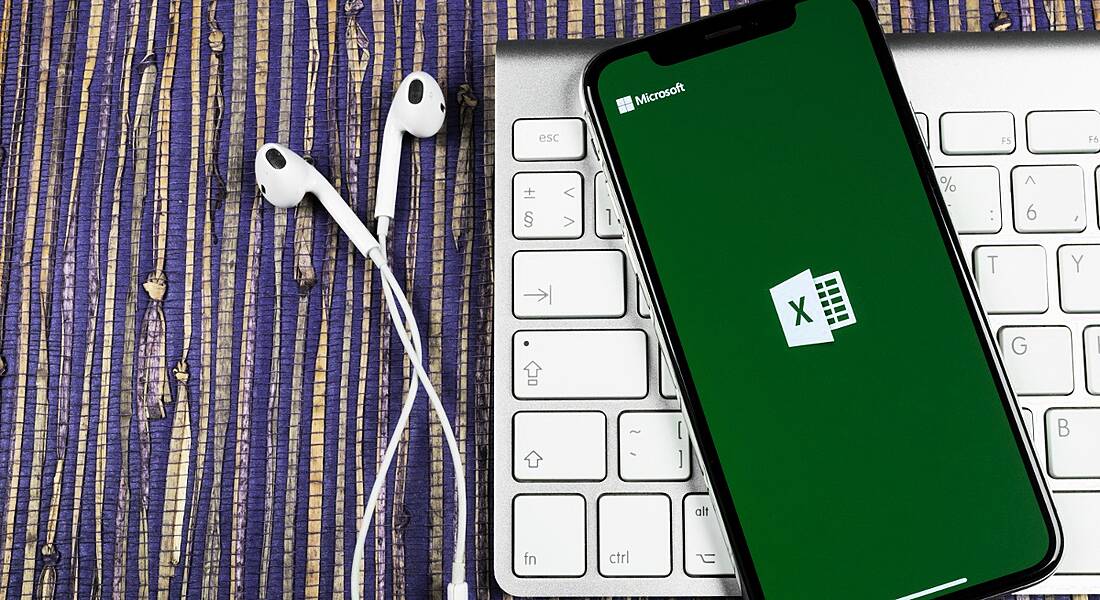 Microsoft Excel application icon on iPhone screen close-up on a striped table cloth and white keyboard.