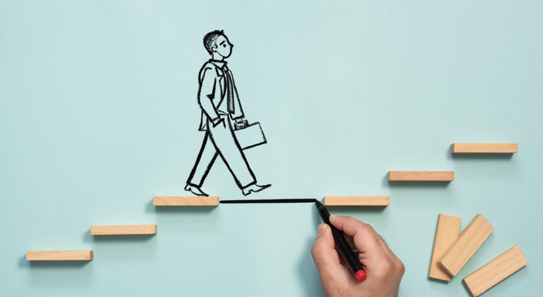 Business person drawn on a blue background with a hand drawing a step to fill a gap in the stairs he is walking up.